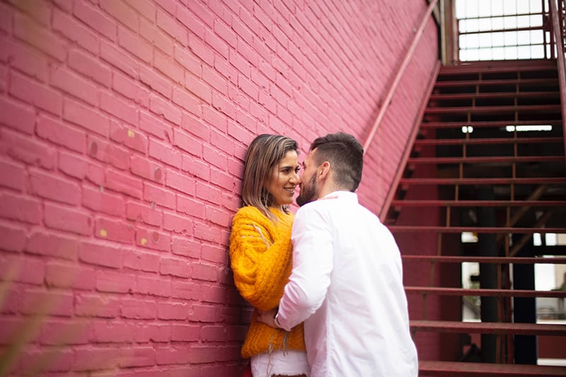 hombre y mujer de pie junto a la pared de ladrillo rojo a punto de besarse