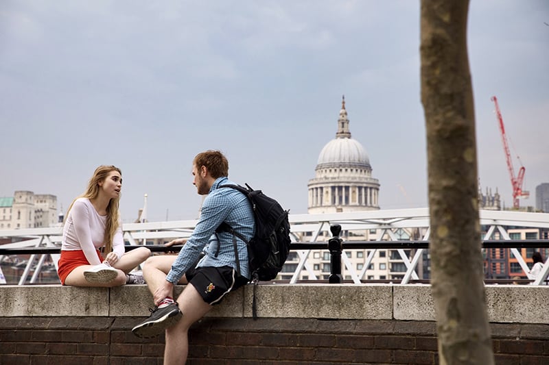 man and woman talking while sitting on concrete wall