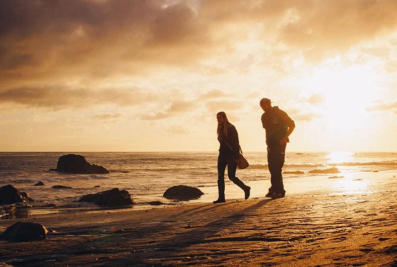 man and woman walking on the seashore during sunset