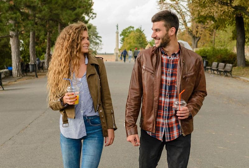 uomo e donna che camminano sui marciapiedi indossando giacche marroni