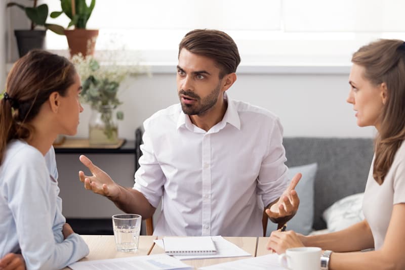 hombre discutiendo con dos mujeres junto a la mesa