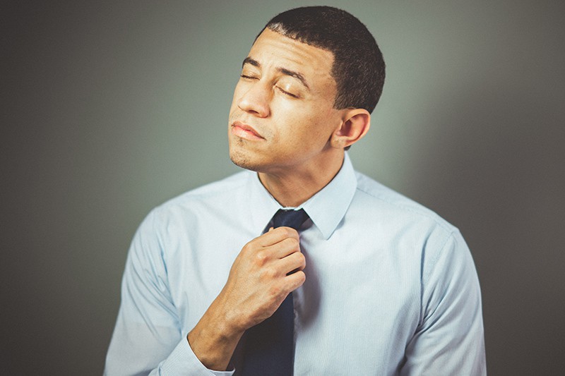 man arranging his black necktie with closed eyes