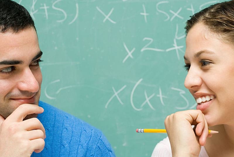 uomo accanto a una donna che tiene una matita con equazioni matematiche alla lavagna dietro di loro