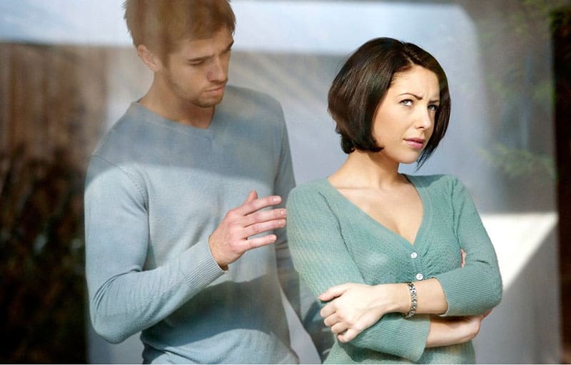 man consoling an angry woman behind big glass windows