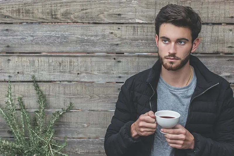 man holding a coffee cup while standing near wooden wall