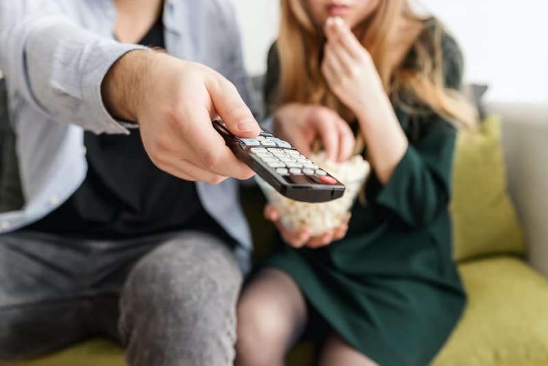 man holding remote control while sitting near woman on couch