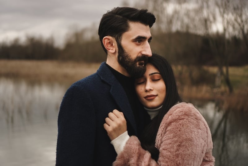 man with beard hugging woman near water