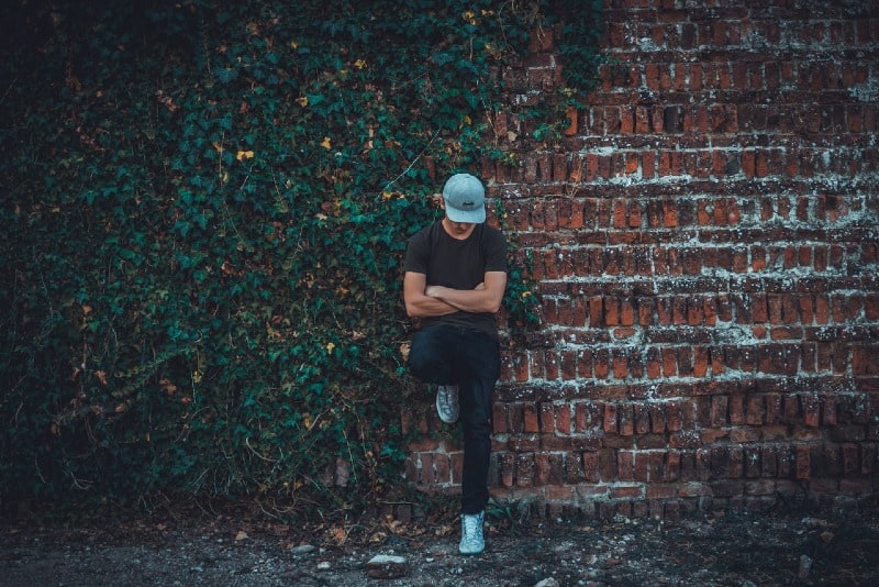 man with cap leaning on brick wall