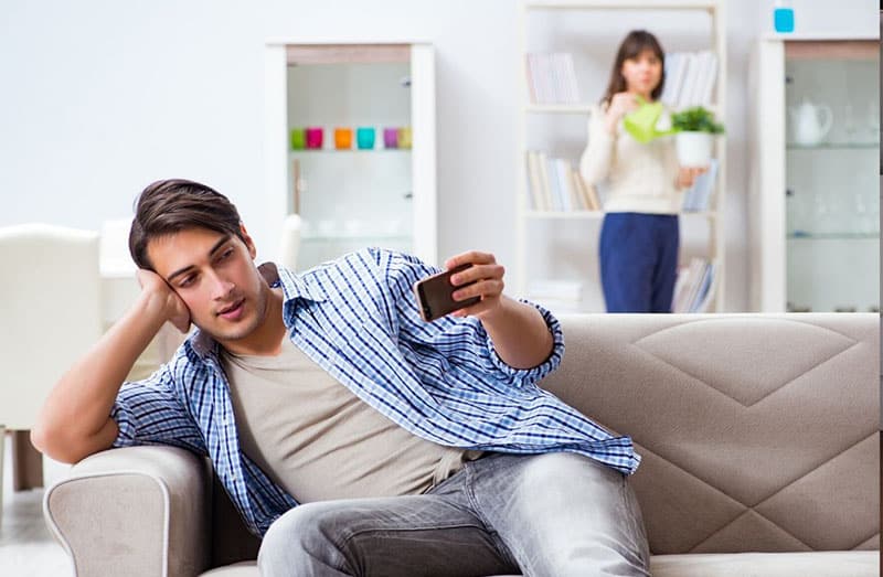 man looking at cellphone with a suspicious wife at a distance