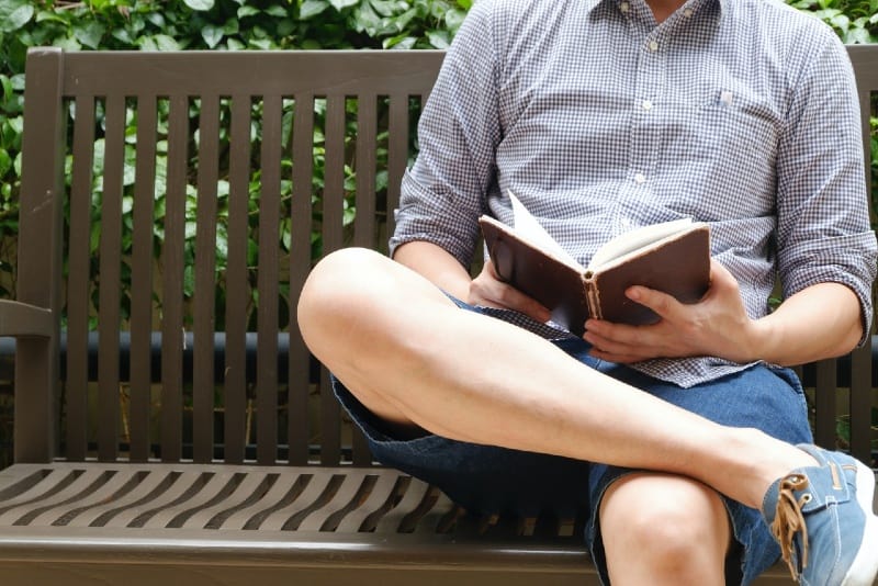 uomo che legge un libro seduto su una panchina