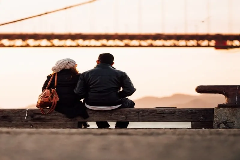 man in black jacket sitting beside woman looking at bridge