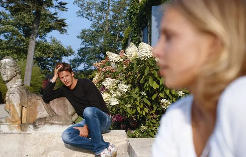 man sitting near the garden staring at a woman in blurred distant from him