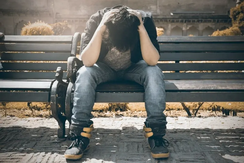 man in black shirt holding his head while sitting on bench