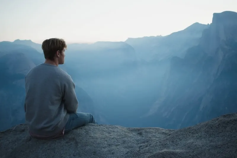 man in gray shirt sitting on cliff