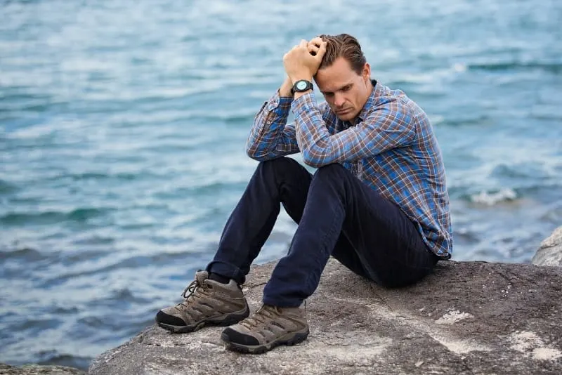 man sitting on rock near water and thinking