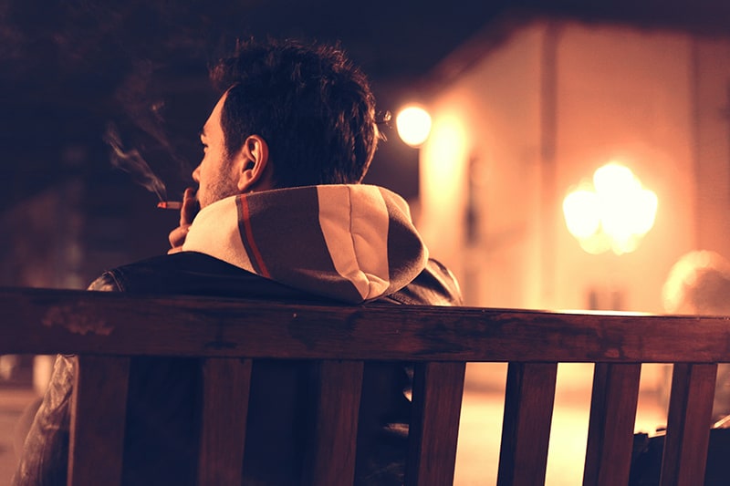 uomo seduto su una panchina mentre fuma una sigaretta