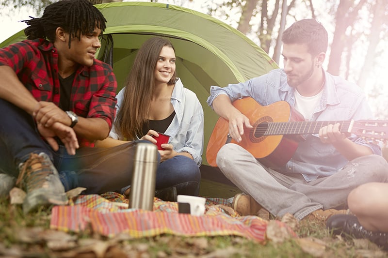 man strumming on acoustic guitar while other man and woman looking him