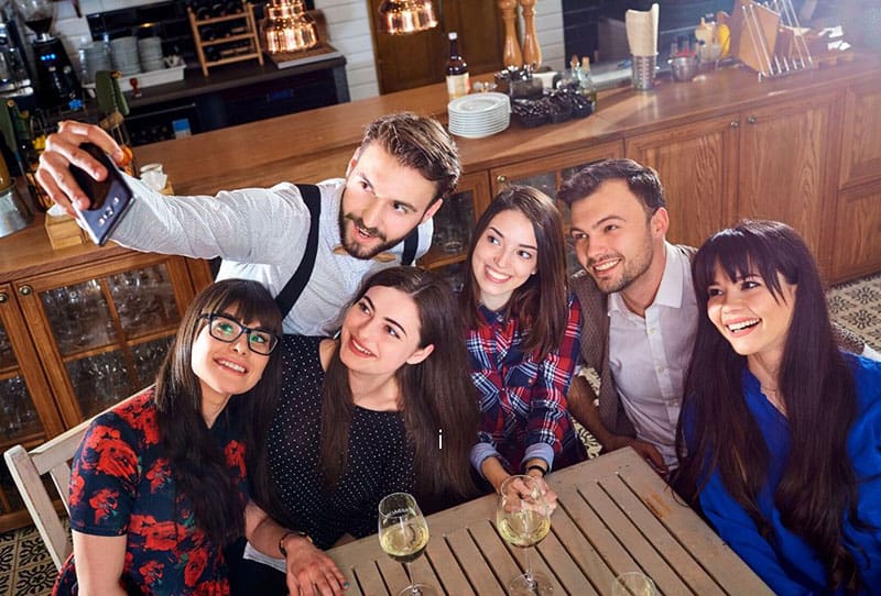 man taking a groufie with friends around the table with few drinks