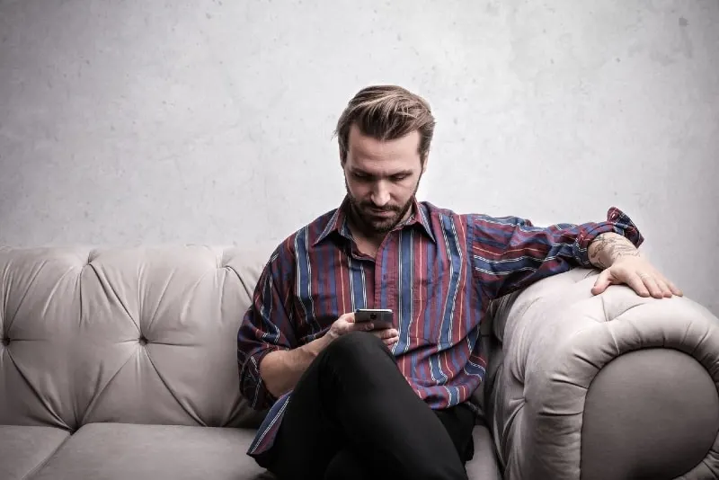 man using smartphone while sitting on white sofa