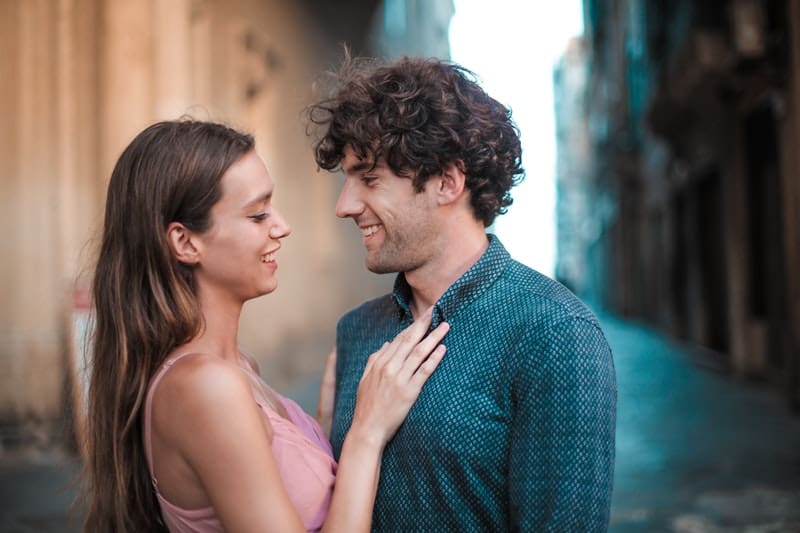 man wearing blue shirt close to woman wearing pink tank touching the man's chest