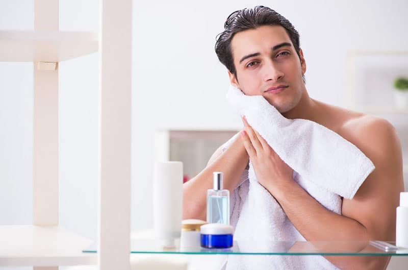 man with a towel wiping his face in front of a mirror