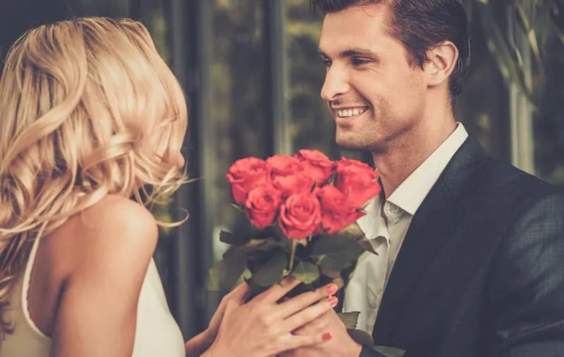 man with bunch of red roses given to a woman in white dress