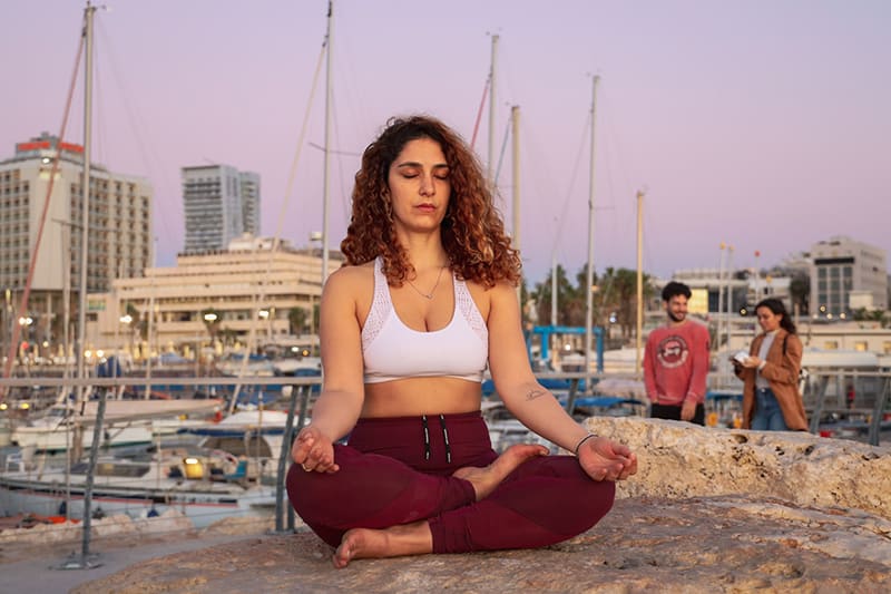 Mulher a meditar com soutien desportivo branco e calças de ioga vermelhas