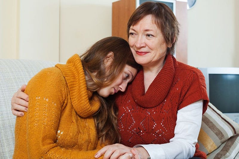 mom hugs daughter while sittiing wearing turtle neck sweaters 