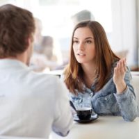 mujer hablando con hombre sentado frente a ella en una mesa