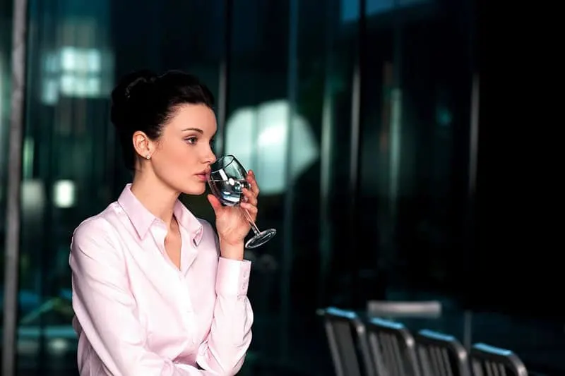 office woman drinking water from a champagne glass inside a a dark theme room