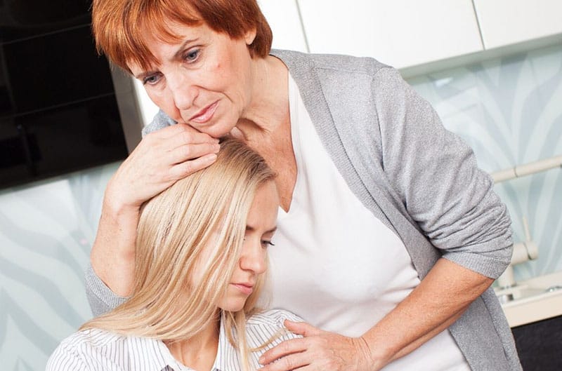 older woman embraces a sad woman with blonde hair sitting and leaning to her chest