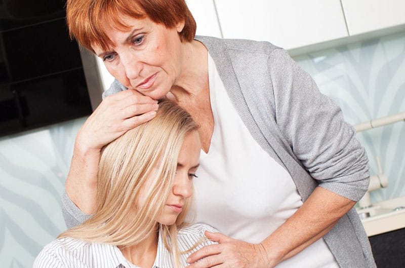 donna anziana abbraccia una donna triste dai capelli biondi seduta e appoggiata al suo petto