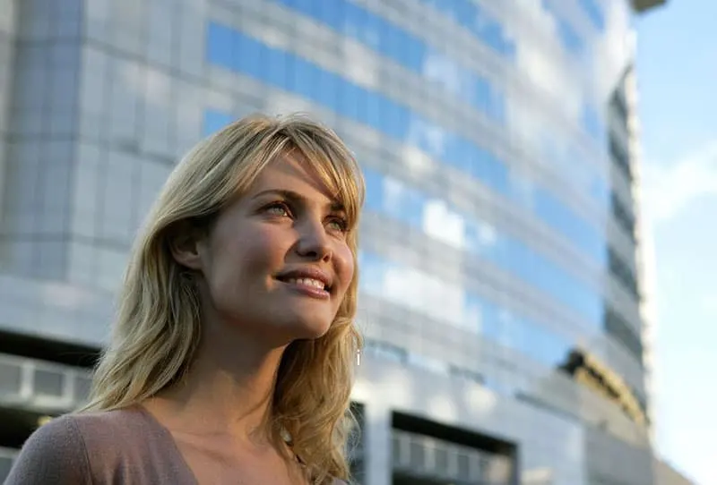 optimist woman smiling somewhere near big glass building