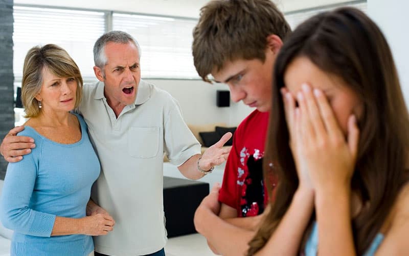 parent scolding teenage son and daughter covering her face