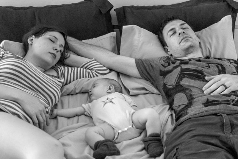 parents and baby sleeping on the bed