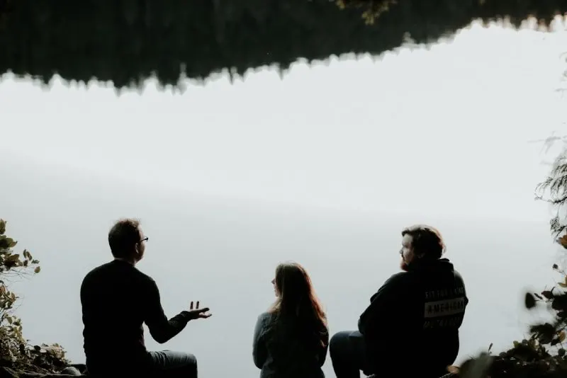 three people sitting near water and talking