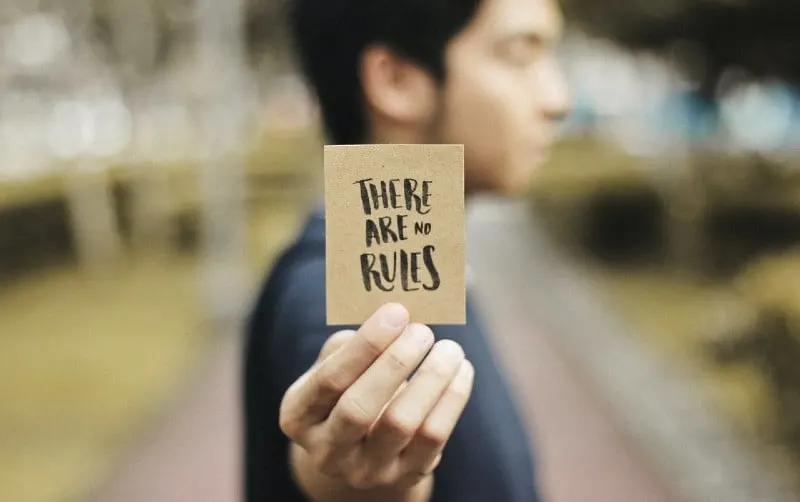 Person holding brown card with There are rules text written on it