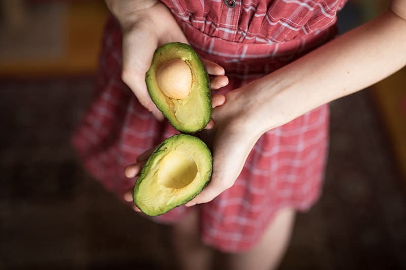 person holding two sliced avocados while standing