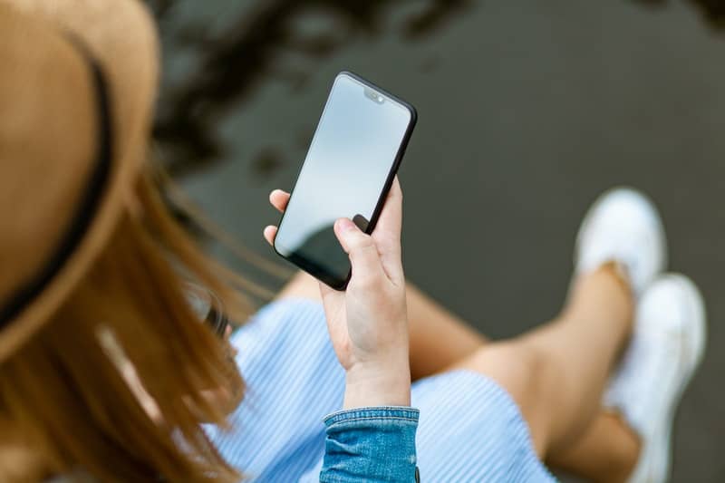 person with hat holding smartphone in a top angle