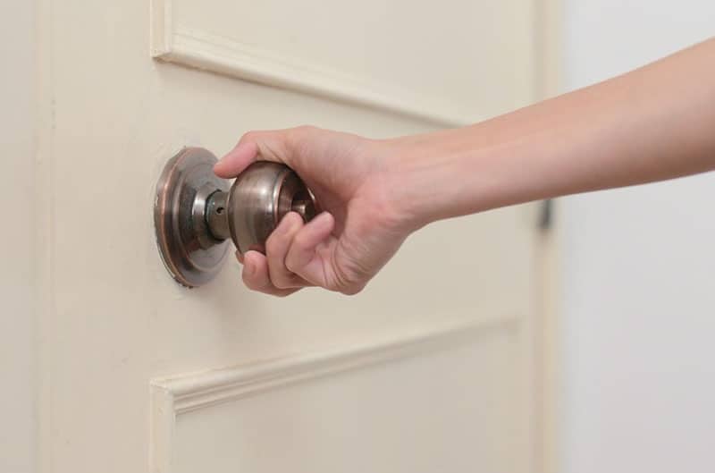 persons hand holding doorknob with dirty white door in focus