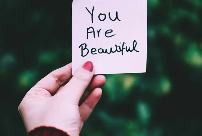 piece of paper with you are beautiful phrase written held by a person with red nail polish