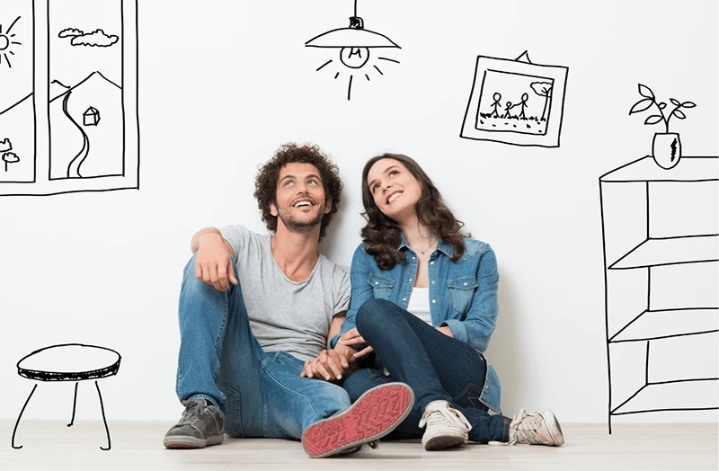 portrait of a young couple sitting on the floor dreaming with drawings of a home essentials around them