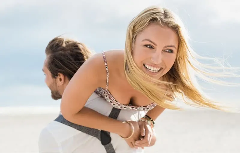 portrait of a young happy couple enjoying outdoors where man piggybacking the woman at the beach