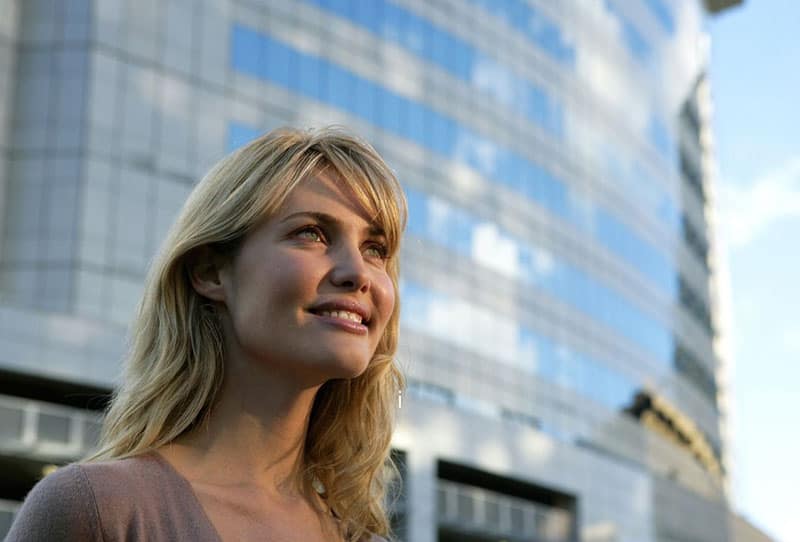 mujer positiva sonriendo y mirando hacia arriba fuera de un edificio 