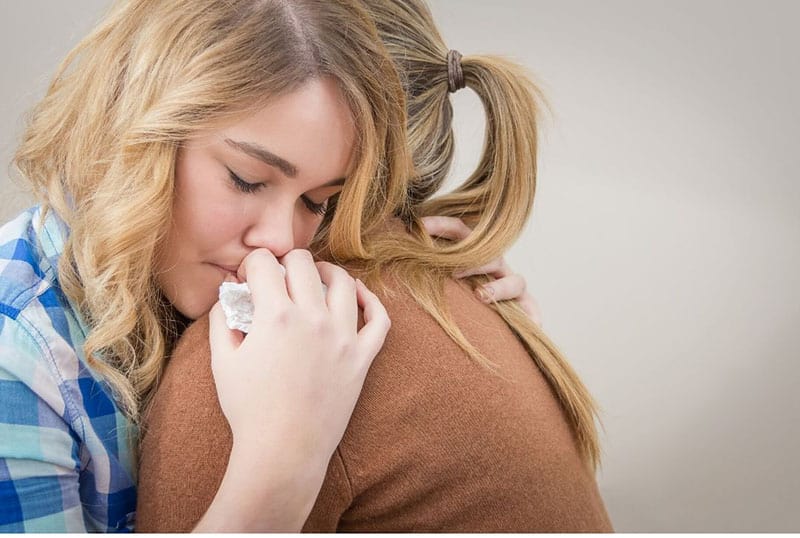 sad woman hugging a woman in brown top