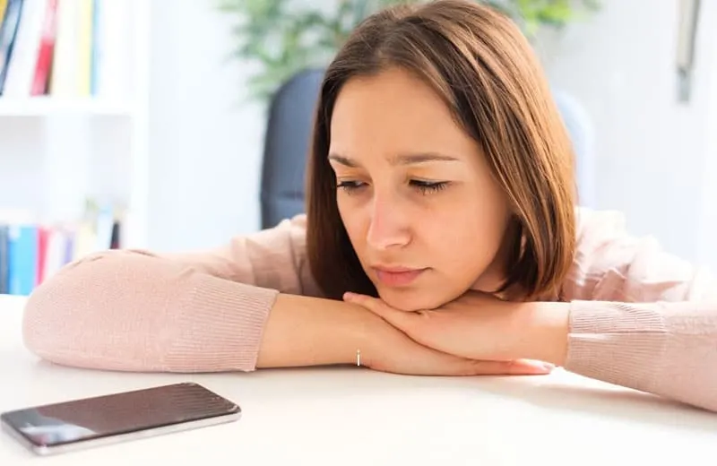 sad woman leaning on the table looking at her cellphone