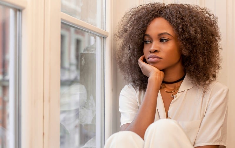 Triste e solitaria donna afroamericana seduta sulla finestra