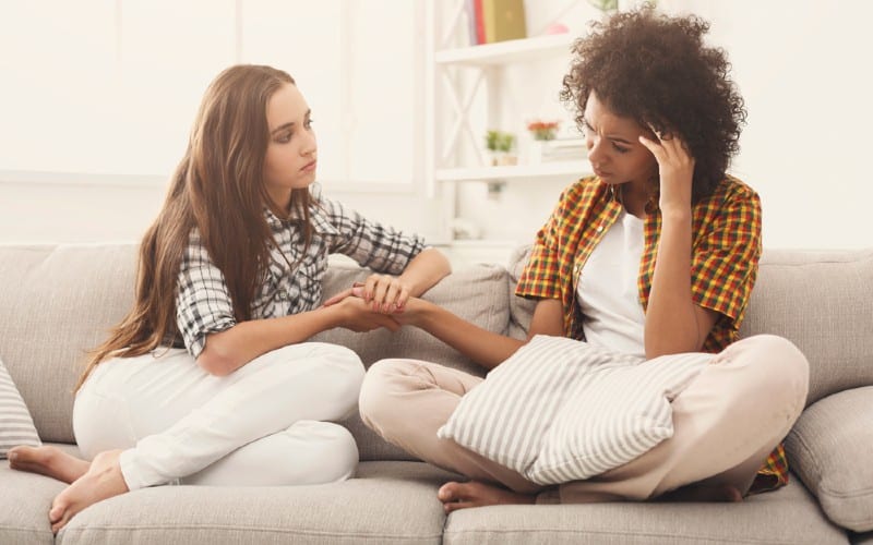 Mulher triste a falar com uma amiga, sentada num sofá branco