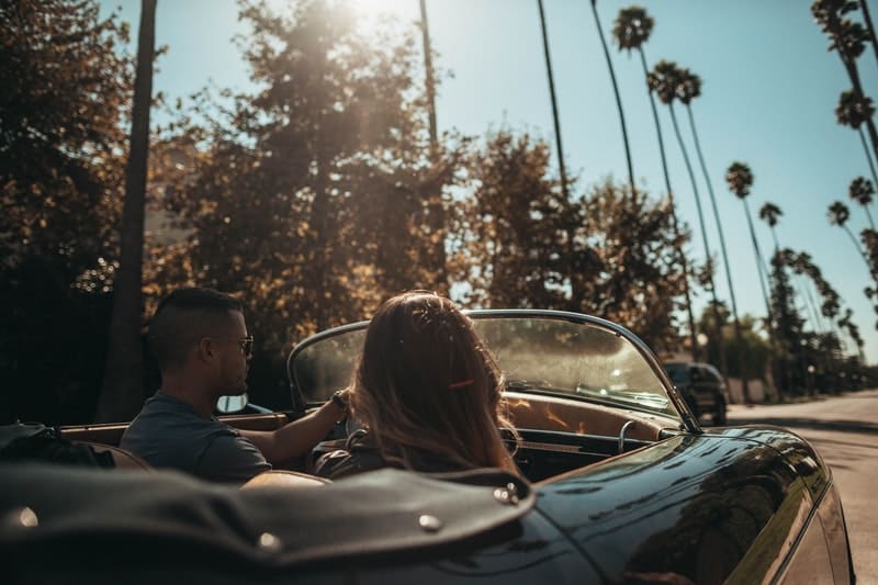 shallow focus photo of people riding in a convertible car in a tropical street
