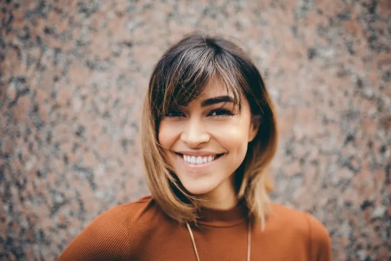 woman in brown top smiling near wall